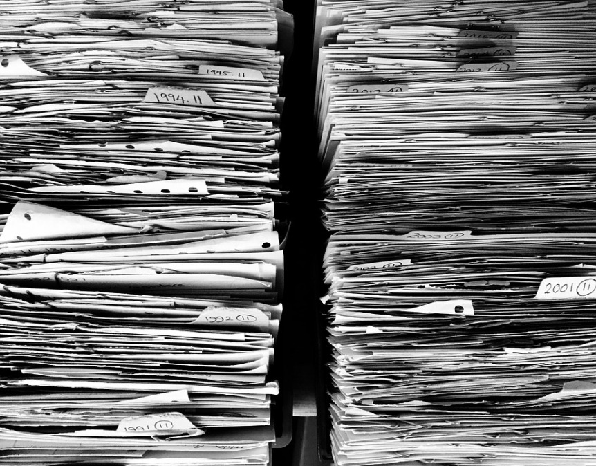 black and white image showing piles of paper files and documents 